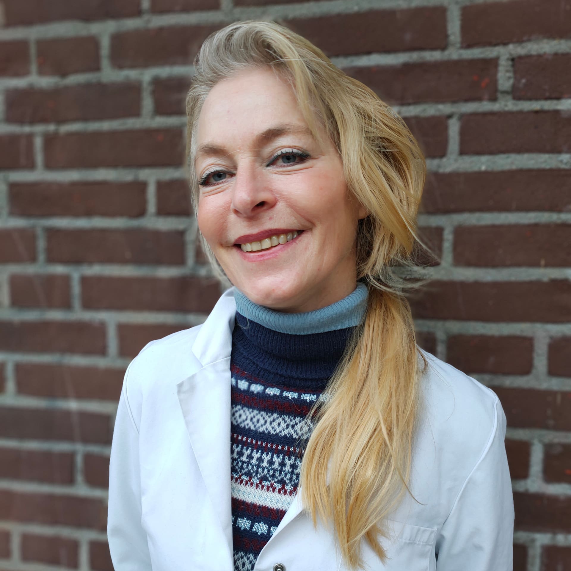 Drs. E. Diepenbroek, dierenarts, in witte jas voor de bakstenen muur bij de kliniek.