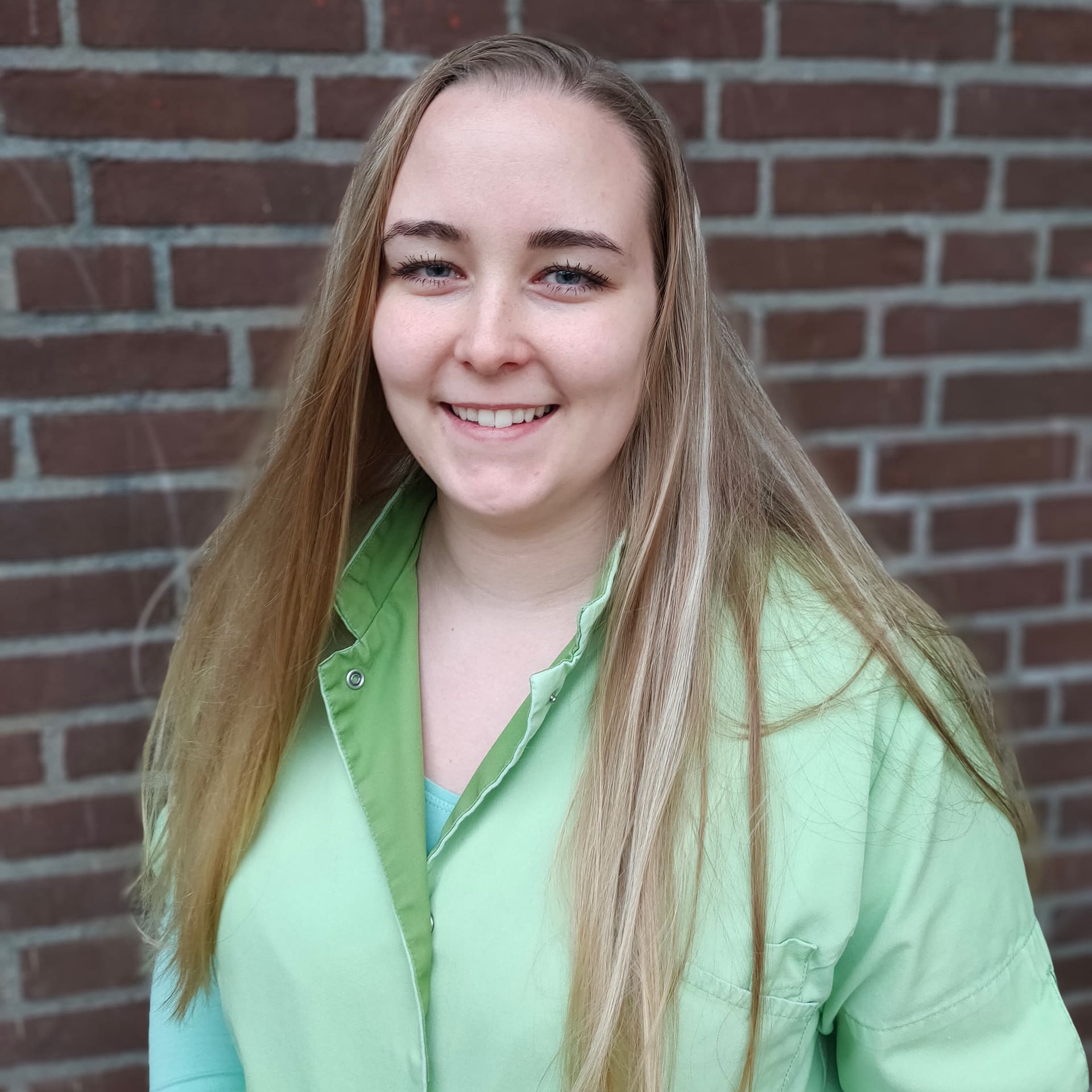 Stephanie van Leijden, paraveterinair, in groene werkkleding voor de bakstenen muur bij de kliniek.
